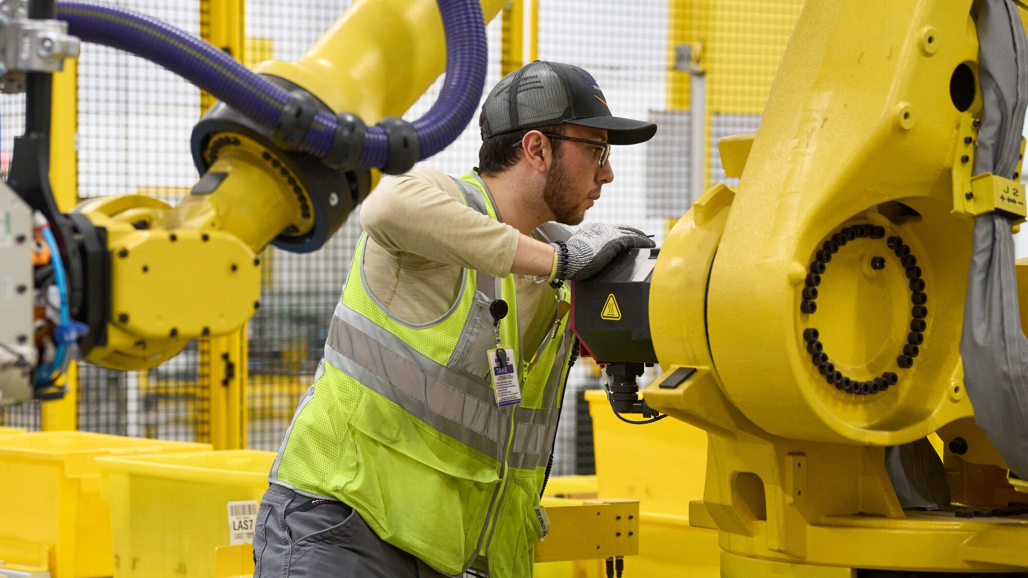 Amazon employee in safety vest maintaining yellow robotic equipment